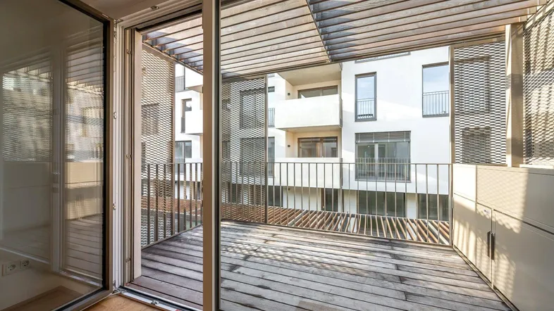 Geräumiger Balkon mit Holzboden und Blick auf die moderne Wohnanlage.