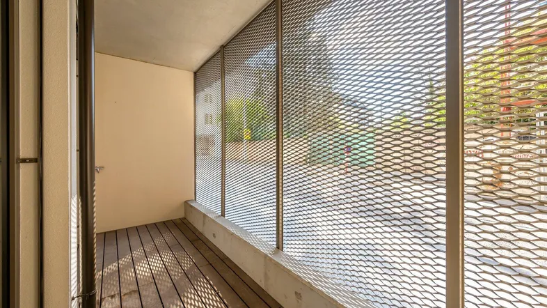Heller Balkon mit Holzfußboden und moderner Metallgitter-Brüstung, bietet Privatsphäre.