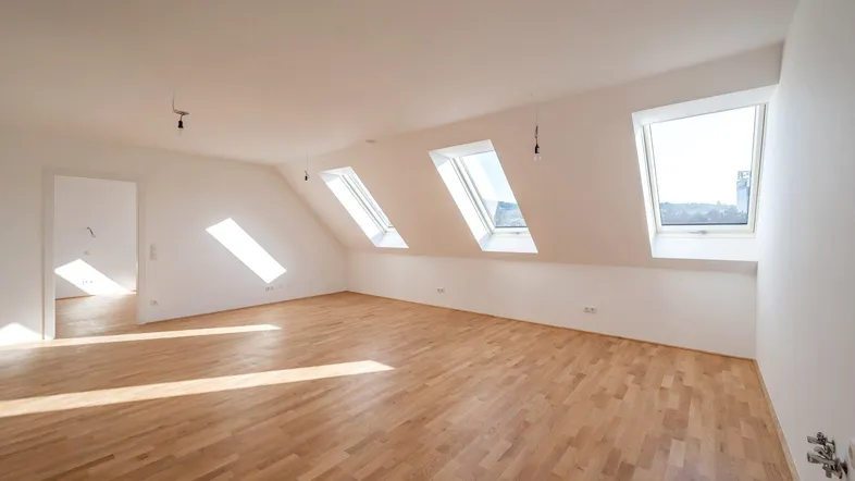 Helles Dachgeschosszimmer mit Holzboden und mehreren Dachfenstern, das viel Tageslicht hereinlässt.