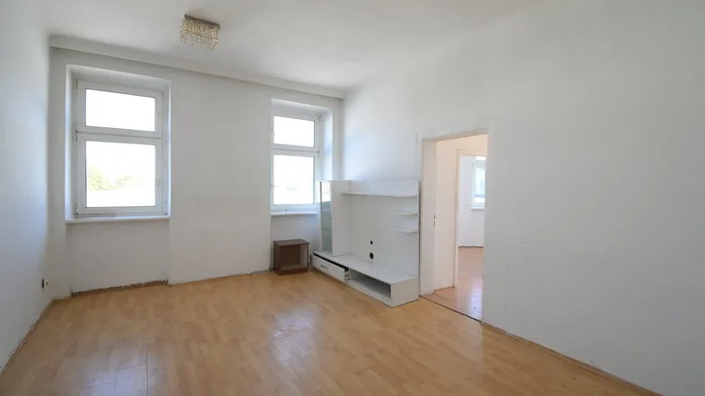 Helles, leeres Wohnzimmer mit Laminatboden und zwei Fenstern, bereit zur individuellen Gestaltung.