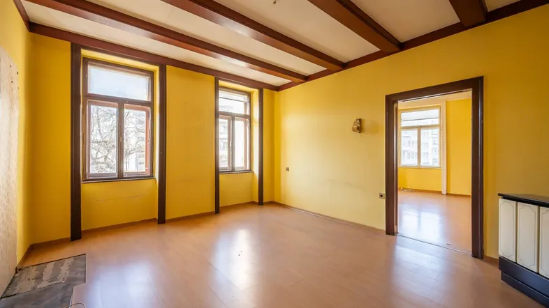 Geräumiges Zimmer mit gelben Wänden, Holzbalkendecke und Laminatboden, bereit zur Renovierung.