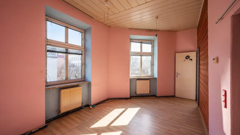 Heller Raum mit rosa Wänden, Holzdecke und Laminatboden, bereit zur Renovierung.