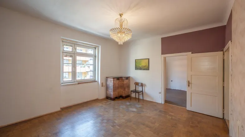 Helles Zimmer mit Parkettboden, Kronleuchter und Blick auf die umliegenden Gebäude.