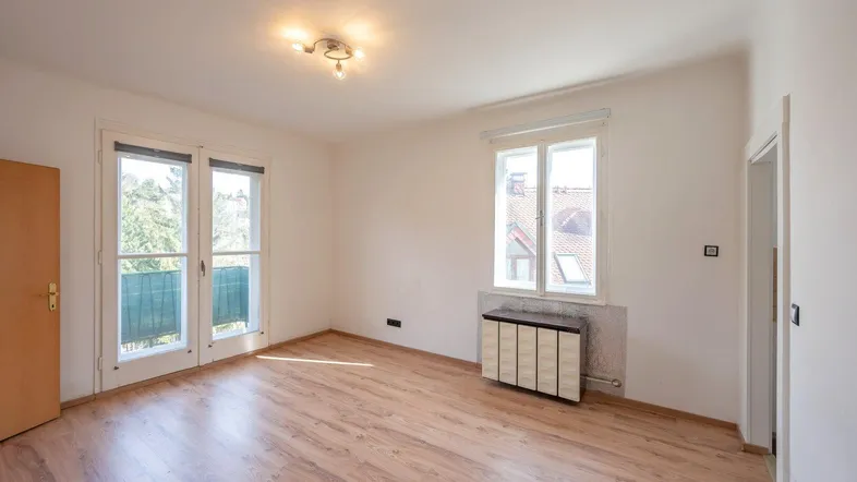 Helles Zimmer mit Laminatboden, Balkonzugang und einem Fenster mit Blick nach draußen.