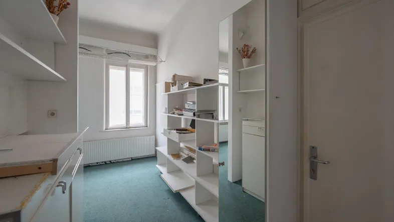 Helles Zimmer mit Teppichboden, Regalen und einem großen Spiegel, ideal als Büro oder Arbeitsbereich.