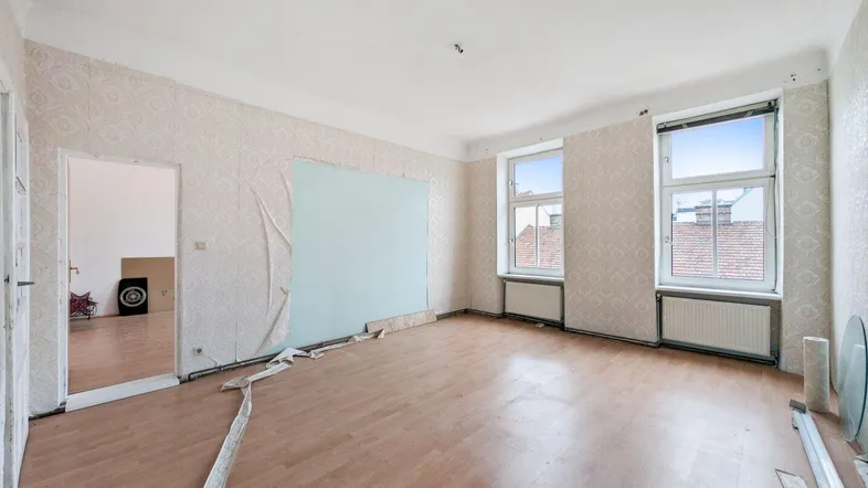 Geräumiges Wohnzimmer mit Laminatboden und Tapetenresten, bereit für eine umfassende Renovierung.