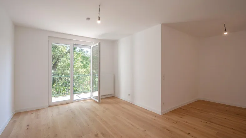 Helles Zimmer mit Holzboden und Zugang zu einem Balkon mit Blick ins Grüne.