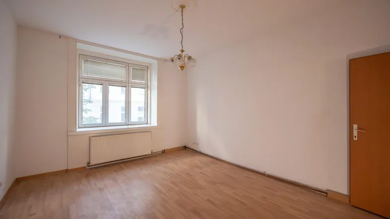 Helles, leeres Zimmer mit Parkettboden und Fenster, bereit für die individuelle Gestaltung.
