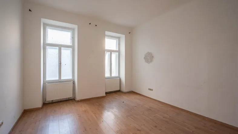 Helles, leeres Zimmer mit Holzfußboden und zwei Fenstern, bereit zur Renovierung.