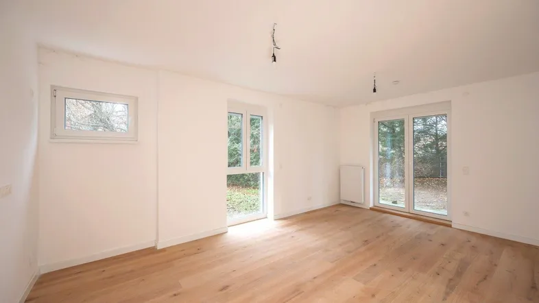 Helles, leeres Zimmer mit Parkettboden und Zugang zum Gartenbereich.