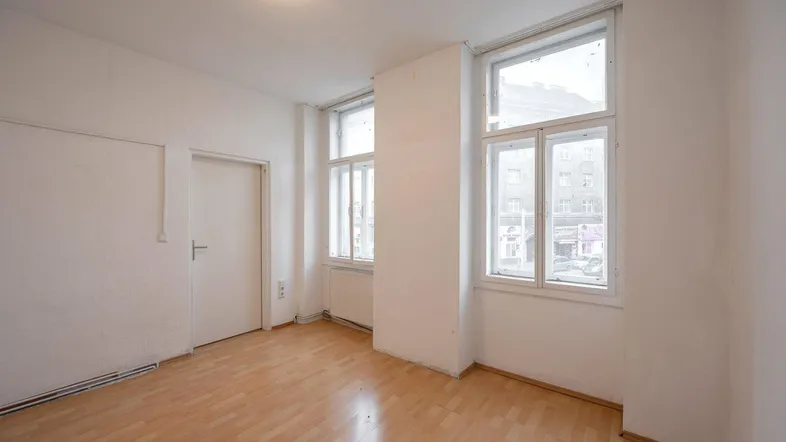 Heller Raum mit Parkettboden und zwei großen Fenstern, die auf die Straße blicken.