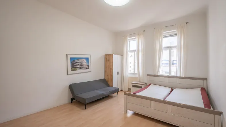 Helles Schlafzimmer mit Doppelbett, Sofa, Kleiderschrank und Parkettboden.