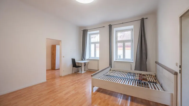 Helles Schlafzimmer mit Holzboden, zwei Fenstern und einem Bettgestell.