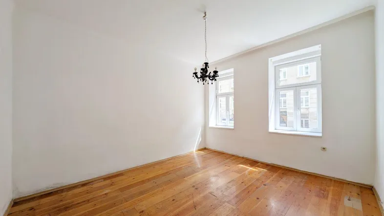 Helles Zimmer mit Holzdielenboden, weißen Wänden und einem eleganten Kronleuchter.