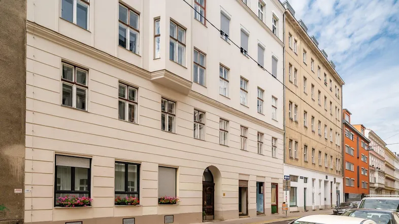 Klassisches Mehrfamilienhaus mit heller Fassade und Fenstern an einer städtischen Straße.