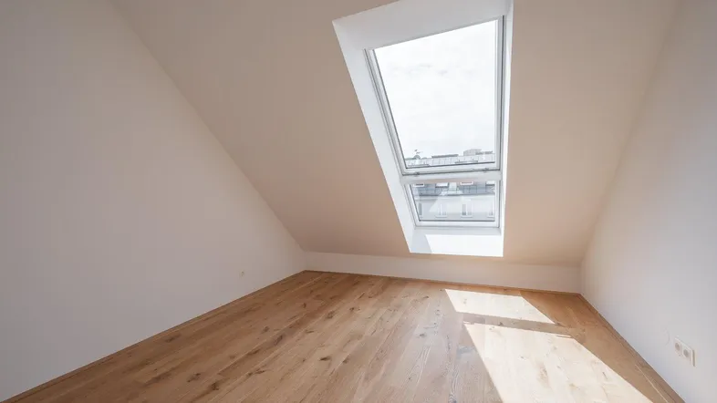 Heller Raum im Dachgeschoss mit Holzboden und großem Dachfenster, das viel Tageslicht hereinlässt.