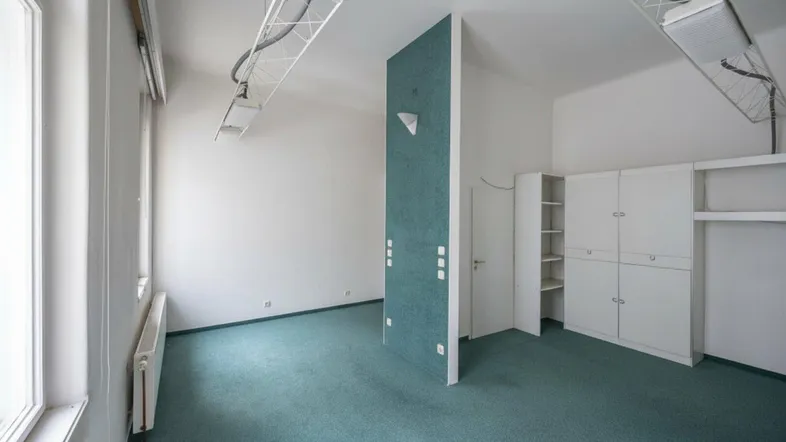 Geräumiger Büroraum mit grünem Teppichboden, weißen Wänden und praktischen Einbauschränken.