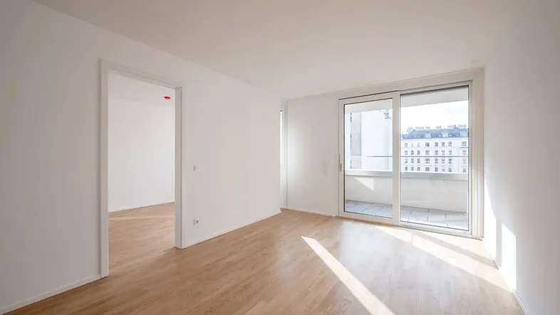 Helles, leeres Zimmer mit Parkettboden und Zugang zu einem Balkon, ideal für Wohnzwecke.