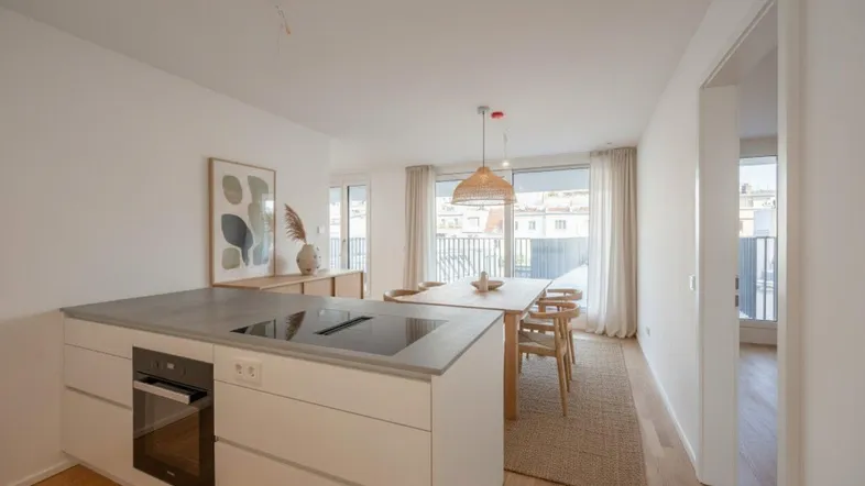 Heller offener Wohn- und Essbereich mit moderner Kücheninsel, Holzboden und Zugang zum Balkon.