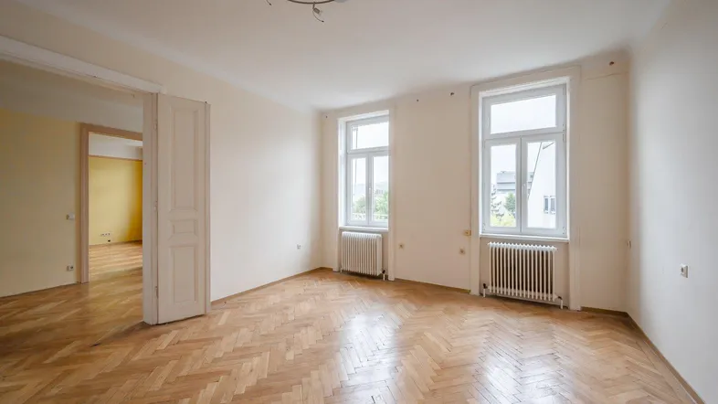 Helles Zimmer mit Fischgrätparkett, hohen Fenstern und Blick ins Grüne.