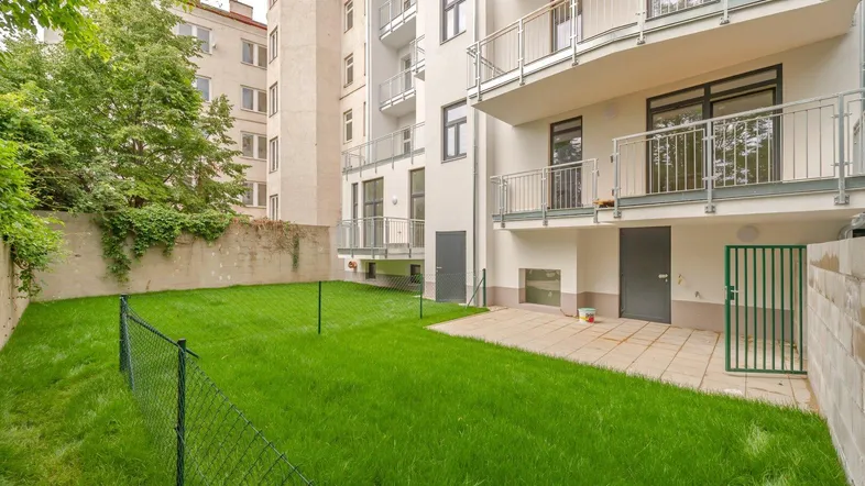 Gepflegter Gartenbereich mit Rasenfläche und kleiner Terrasse hinter dem Wohngebäude.