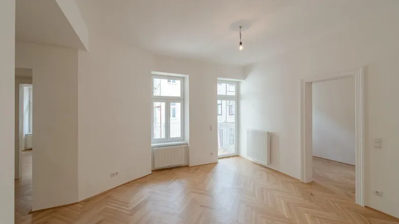 Helles, frisch renoviertes Zimmer mit Fischgrätparkett und Zugang zu einem französischen Balkon.