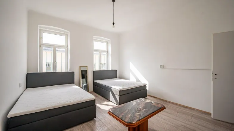 Helles Schlafzimmer mit zwei Betten, Holzboden und großen Fenstern, die viel Tageslicht hereinlassen.