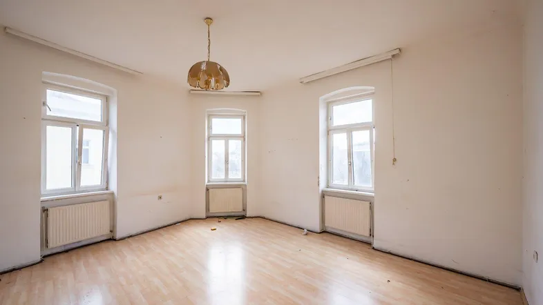 Geräumiger, unmöblierter Raum mit Laminatboden und mehreren Fenstern, der Renovierung bedarf.