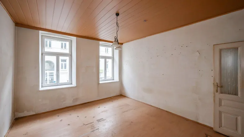 Leerer Raum mit Holzdeckenverkleidung, Holzboden und zwei Fenstern zur Straße.