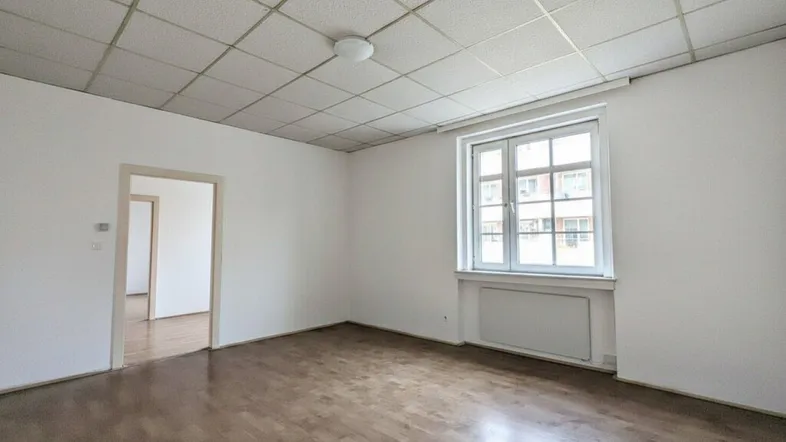 Helles, leeres Zimmer mit Holzfußboden, weißen Wänden und einem Fenster.