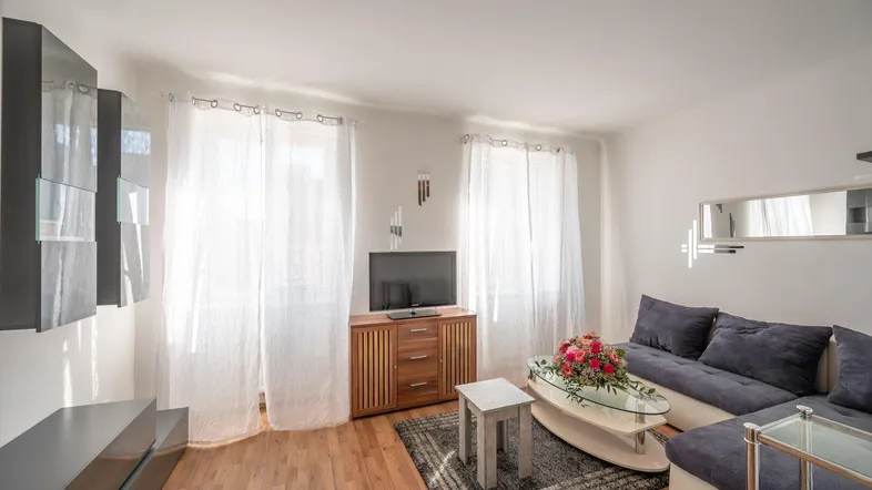 Helles Wohnzimmer mit bequemer Couch, Holzboden und viel Tageslicht durch große Fenster.