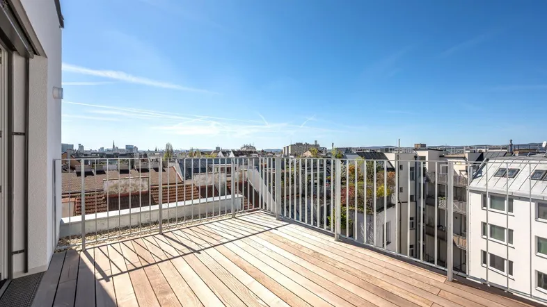 Geräumige Dachterrasse mit Holzboden und weitem Blick über die Stadt unter blauem Himmel.