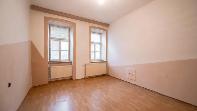 Helles Zimmer mit Holzfußboden und zwei Fenstern, bereit zur individuellen Gestaltung.