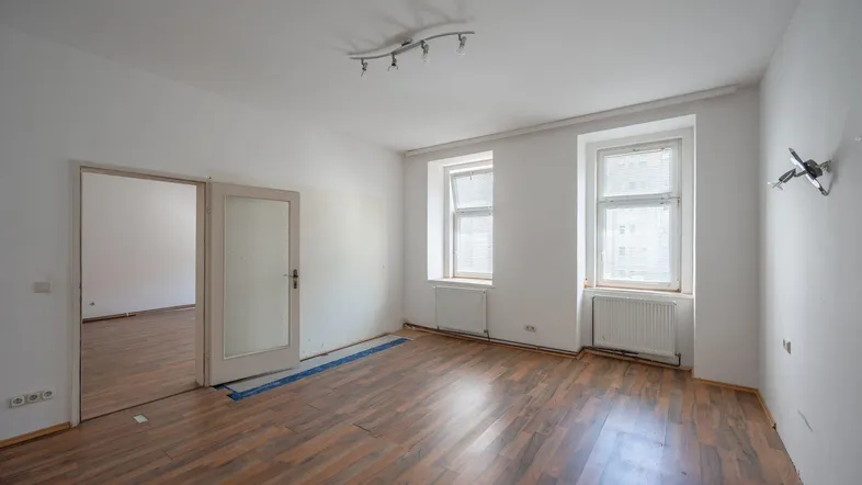 Helles, leeres Zimmer mit Holzboden und zwei Fenstern, bereit zur Renovierung.