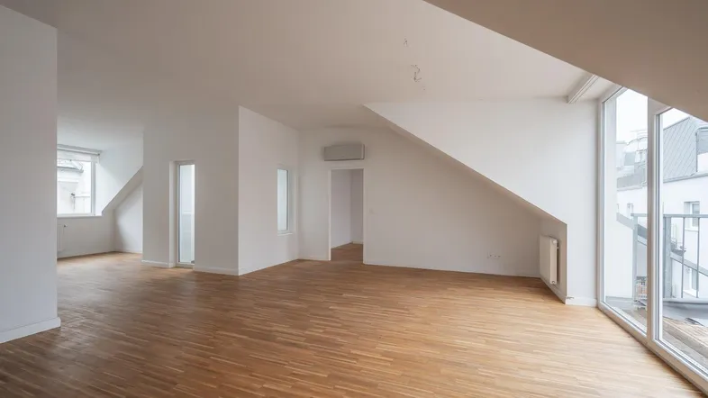 Helles, geräumiges Wohnzimmer mit Parkettboden, Dachschrägen und Zugang zu einem kleinen Balkon.