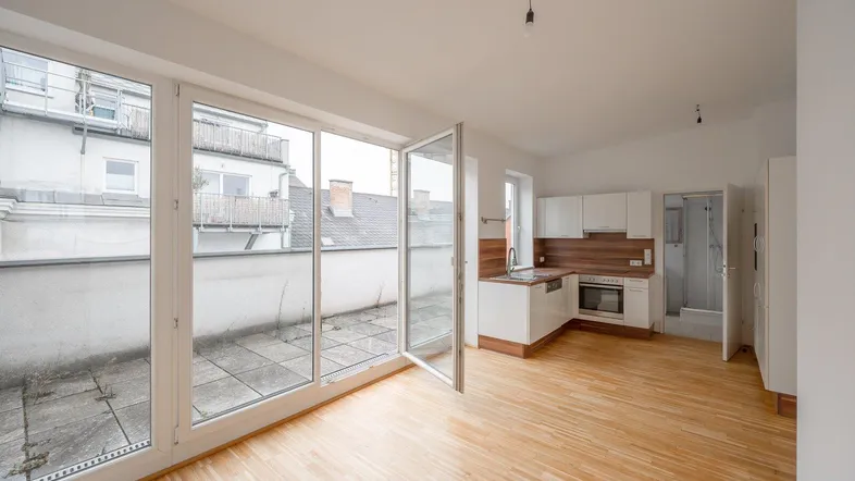 Heller offener Wohnbereich mit integrierter Küche, Holzboden und Zugang zu einer großen Terrasse.