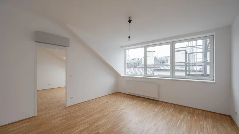 Helles Zimmer mit Dachschräge, Parkettboden und Klimaanlage in einem Neubau.