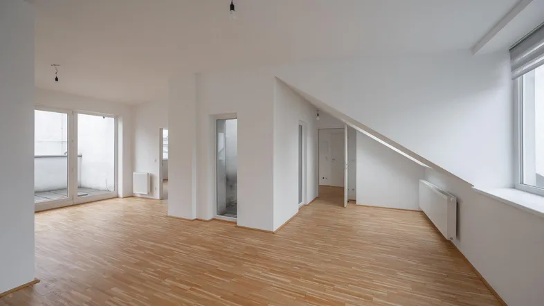 Helles, offenes Zimmer mit Parkettboden und Zugang zu einem Balkon oder einer Terrasse.