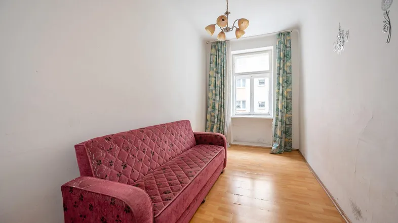 Helles Zimmer mit rotem Sofa, Holzfußboden und einem Fenster mit Vorhängen, das auf die Straße blickt.