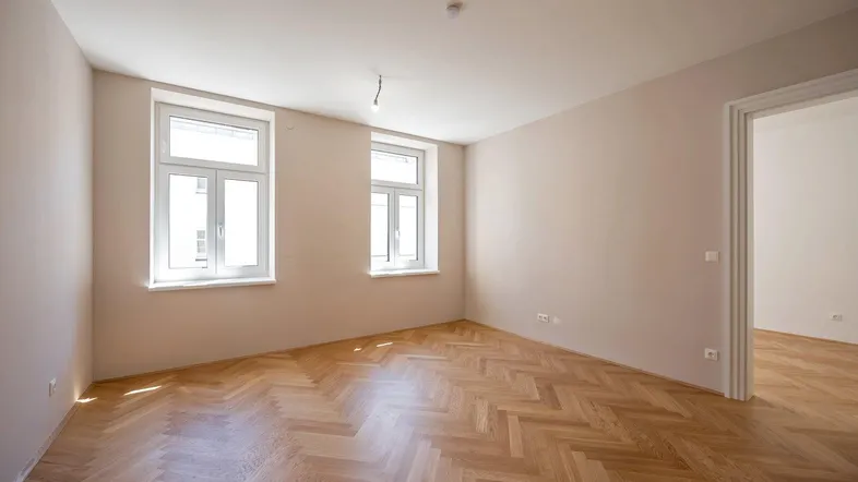 Helles Zimmer mit Fischgrätparkett und zwei großen Fenstern, bereit zur individuellen Gestaltung.