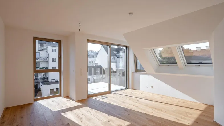 Helles Wohnzimmer mit Holzboden, großen Fenstern und Zugang zum Balkon. Dachfenster sorgen für zusätzliches Licht.