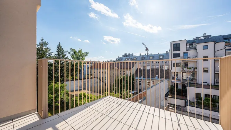 Heller Balkon mit Fliesenboden und Blick über die Stadt unter blauem Himmel.