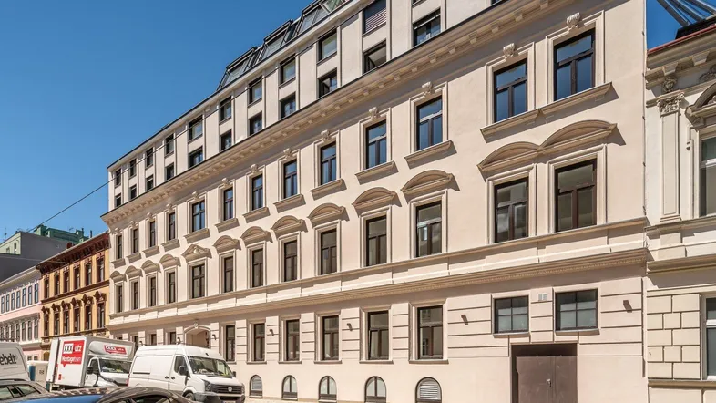 Klassisches Mehrfamilienhaus mit eleganter Fassade und vielen Fenstern an einem sonnigen Tag.