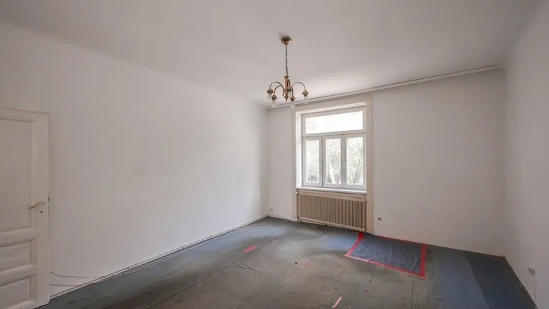 Helles Zimmer mit Fenster, Kronleuchter und vorbereitetem Boden für neue Beläge.