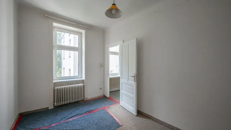 Leeres Zimmer mit Fenster, Heizkörper und Teppichboden, bereit für Renovierung.