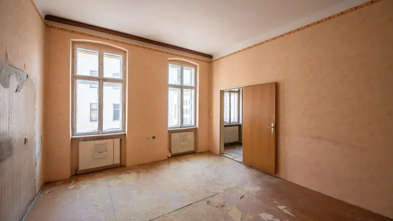 Leerer Raum mit abblätternder Tapete und beschädigtem Boden, bereit für eine umfassende Renovierung.