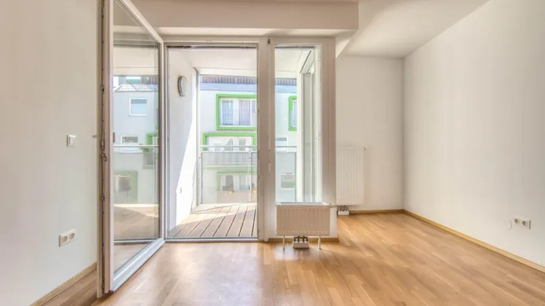 Helles Zimmer mit Parkettboden und großen Glasfronten, die Zugang zu einem Balkon bieten.