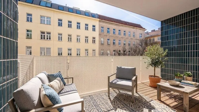 Möblierter Balkon mit Holzboden, Sitzgelegenheiten und Blick auf die umliegenden Gebäude.