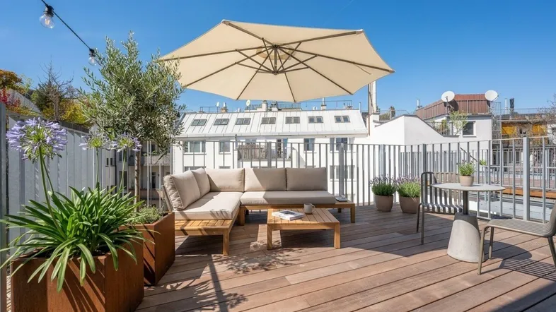 Möblierte Dachterrasse mit bequemen Sitzgelegenheiten, Sonnenschirm und Pflanzen unter blauem Himmel.
