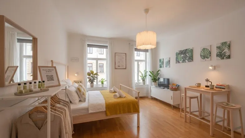 Helles Schlafzimmer mit Holzboden, Doppelbett, Esstisch und großen Fenstern, modern eingerichtet.